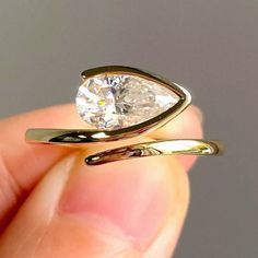 a hand holding a gold ring with a white diamond in it's center and two curved bands around the band