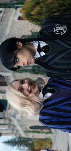 two young women standing next to each other in front of a building and looking at the camera