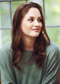 a woman sitting in front of a window with her arms crossed and looking off to the side