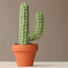 a crocheted cactus sits in a pot on a table next to a wall