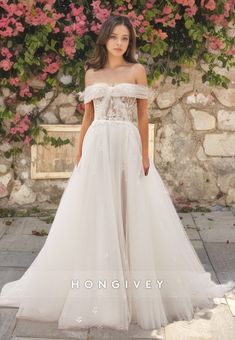 a woman in a white wedding dress standing on a stone walkway with pink flowers behind her