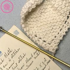 a knitted hat next to a crochet hook and paper with writing on it