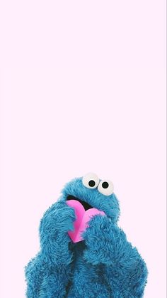 a blue stuffed animal holding a pink heart in it's mouth and looking at the camera