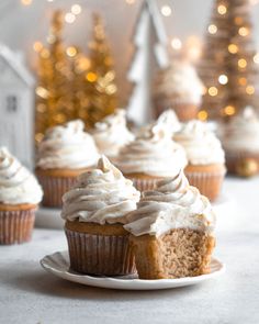 cupcakes with white frosting on a plate next to small trees and christmas lights