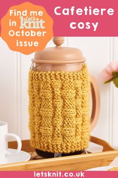 a knitted coffee pot cozy sitting on top of a wooden tray next to a mug