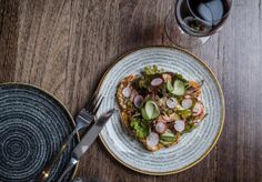 a white plate topped with food next to a glass of wine on top of a wooden table