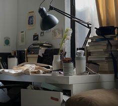 a desk with a lamp, books and other items on it in front of a window