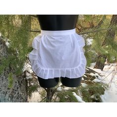 a mannequin wearing a white ruffled skirt in front of snow covered trees