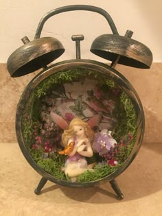 an alarm clock with a fairy figurine in the center and flowers around it