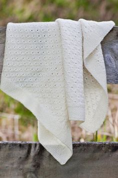 a white knitted blanket hanging on a wooden fence