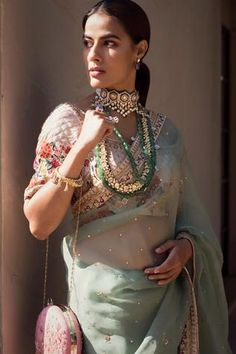 a woman in a green sari with jewelry on her neck and hands behind her back