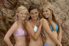 three beautiful young women in bikinis standing next to a rock wall and posing for the camera