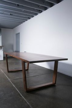 a wooden table sitting on top of a cement floor next to a white wall in an empty room