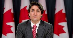 a man in a suit and tie sitting at a table with canadian flags behind him