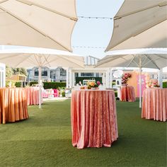 an outdoor event with tables covered in pink and orange cloths, chairs and umbrellas