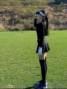 a woman wearing a skirt and blindfold is standing in the grass with her hand on her head