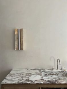 a marble counter top in a bathroom with two faucets on the wall and a mirror above it