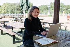 a woman sitting at a picnic table with a laptop computer in front of her,