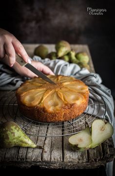 a person cutting into a cake on top of a cooling rack next to pears