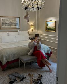 a woman in a red dress sitting on a bed next to a teddy bear and shoes