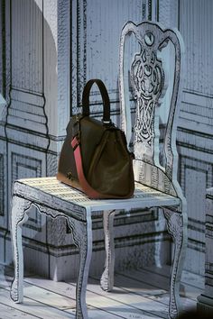 a brown purse sitting on top of a wooden chair next to a white table and chairs