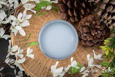 a wicker basket filled with white flowers and a blue candle surrounded by pine cones