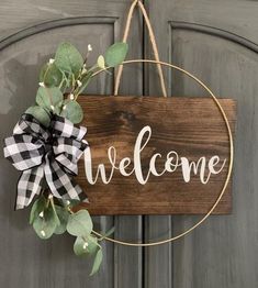 a welcome sign hanging on a door with greenery in the foreground and a black and white checkered ribbon tied to it