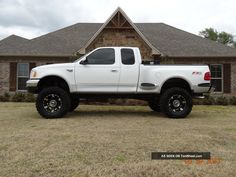 a white pickup truck parked in front of a house with large tires on it's flatbed