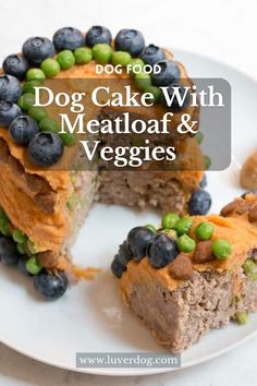 dog cake with meatloaf and veggies is on a white plate next to some blueberries