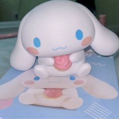 a white toy with blue eyes sitting on top of a table next to a book