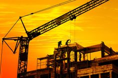 two construction workers are working on the top of a building under construction at sunset or dawn