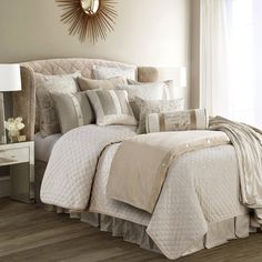 a bed with white and beige comforters in a bedroom next to a lamp on a table