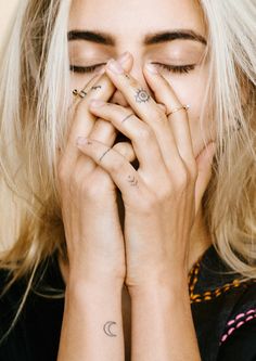 a blonde woman with tattoos covering her face and hands, holding her hand to her mouth