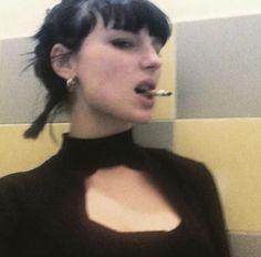 a woman with black hair is brushing her teeth in front of a tiled bathroom wall