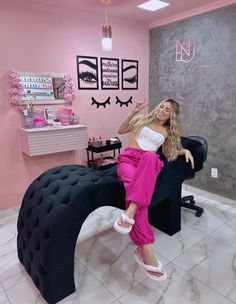 a woman sitting on top of a black chair in a pink and white salon room