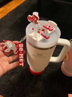 a person holding a coffee mug with some decorations on it and two key chains attached to the cup