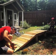 two men working on a wooden ramp in the yard with bikes behind them and another man standing next to it