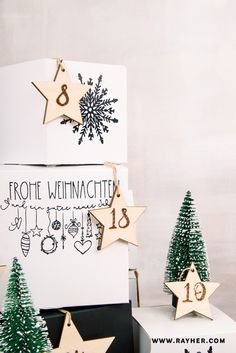 three wooden christmas trees on display in front of a white box with black and gold decorations