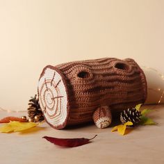 a crocheted log sitting on top of a table next to leaves and pine cones