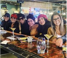 a group of women sitting at a bar posing for the camera with drinks in front of them