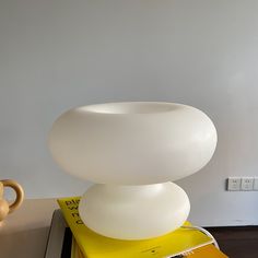 a large white vase sitting on top of a stack of books next to a cup