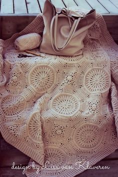 a crocheted blanket and purse sitting on a wooden bench next to a handbag