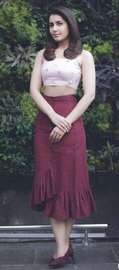 a woman standing in front of a green wall wearing a red skirt and crop top