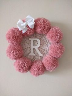 a pink pom - pom wreath with the letter r on it and a white bow