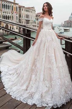 a woman in a wedding dress standing on a bridge near the water with buildings behind her