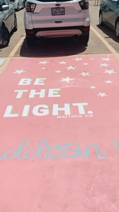 a pink parking lot with white stars painted on it and the words be the light written in blue