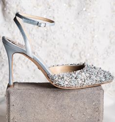 a pair of silver high heeled shoes sitting on top of a cement block in front of a white wall