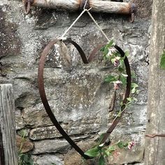 a heart shaped metal object hanging from a wooden pole next to a stone wall with vines growing on it