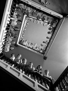 black and white photograph of people looking up at the ceiling in a room filled with dolls