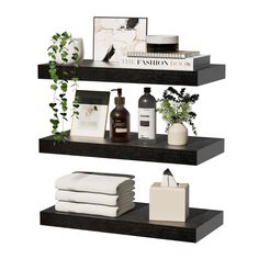 three black shelves with white towels, plants and other items on top of each shelf